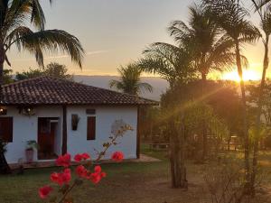 Una pequeña casa blanca con palmeras y la puesta de sol. en Pousada da Lua, en Delfinópolis