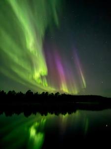 an aurora over a lake with a reflection in the water at Lapland Apartments with sauna and free WiFi and parking in Rovaniemi