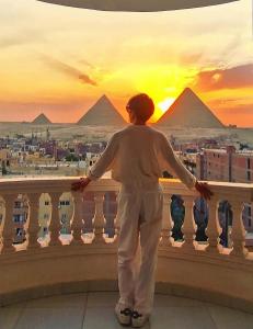 a man standing on a balcony looking at the pyramids at Pyramids Suite in Cairo