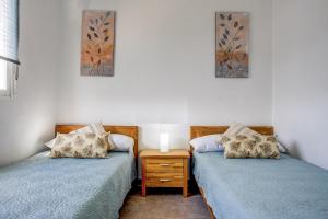 zwei Einzelbetten in einem Zimmer mit Nachttisch und Gemälden in der Unterkunft Jardines de Denia in Denia