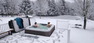 Due persone sedute in una vasca idromassaggio nella neve di Mountain Blue Vista - Luxury retreat near Ski resorts with Pond, Firepit and Hot Tub a Windham