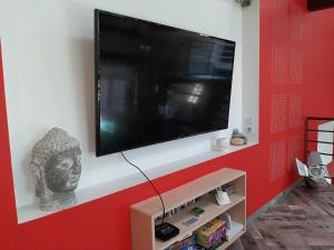un téléviseur à écran plat sur un mur rouge avec une statue dans l'établissement La clé des Champs, à Roche