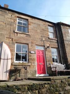 a brick building with a red door and a bench at Rose Lea, Beautiful Seaside Home in Staithes
