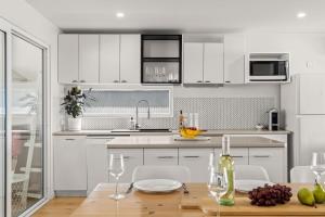 a kitchen with white cabinets and a wooden table with wine glasses at Flatrock Penthouse Ulladulla in Ulladulla