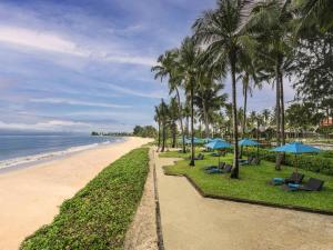 a beach with palm trees and blue umbrellas at Grand Mercure Khao Lak Bangsak in Khao Lak