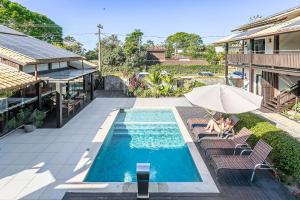 a person sitting under an umbrella next to a swimming pool at Pousada Rosa 08 - Café da manhã Gourmet, Suítes com Banheira a 150m do Centrinho da Praia do Rosa in Praia do Rosa