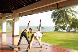 two people performing a yoga pose in front of the ocean at Jetwing Lagoon Wellness, A Luxury Reserve - Adults Only in Negombo