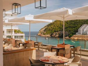 um restaurante com mesas e guarda-sóis brancos e o oceano em Hyde Ibiza em Cala Llonga