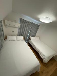 zwei Betten in einem Zimmer mit weißen Laken in der Unterkunft さくら旅館 吉祥寺千利休301号室 in Musashino