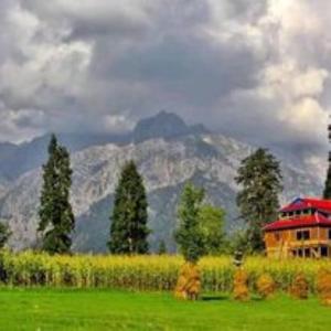 a house in a field with a mountain in the background at Hotel Rest Inn in Dargai