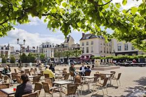 persone sedute ai tavoli in un cortile con edifici di L'Appartement du Forum - Reims centre Cathédrale a Reims