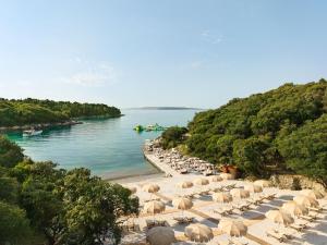 una playa con sillas y sombrillas junto al agua en Arba Resort, Valamar Collection, en Rab