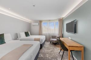 a hotel room with two beds and a desk and a tv at Hotel Elms Christchurch, an Ascend Collection Hotel in Christchurch