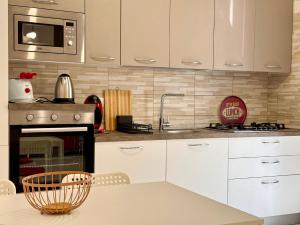 a kitchen with white cabinets and a sink and a microwave at Da Nonna Concetta - 5 minutes walk from the beach in Donnalucata