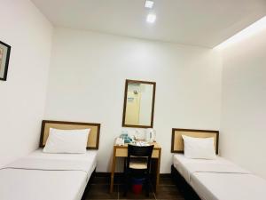 two beds in a room with a table and a mirror at Hotel Sunflower - HLS in Malacca