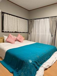 a bedroom with a large bed with blue sheets and pink pillows at 岳見の宿 天然温泉とプライベートサウナの一棟貸しヴィラ in Yufuin