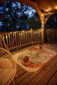 a man and a woman in a hot tub on a deck at Domaine de Pech et Lafon Cabanes avec SPA privatif dans les arbres in Clairac