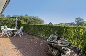 a patio with a table and chairs next to a hedge at Ferienwohnung Ingwersen Nordstrand in Nordstrand