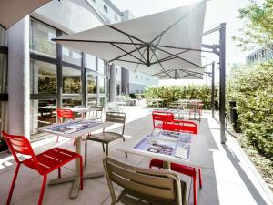 ルクセンブルクにあるIbis Luxembourg Airportの赤い椅子とテーブル、白い傘のあるパティオ