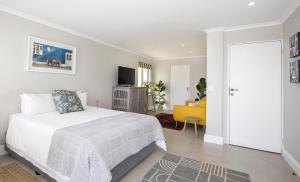 a white bedroom with a bed and a yellow chair at LIMA HOUSE, Seaforth, Simon's Town in Simonʼs Town