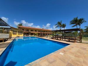 a large swimming pool with benches and a building at Pousada Costa do Sol in Canavieiras