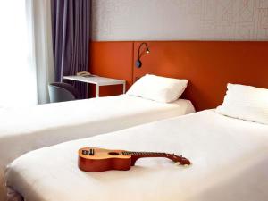 a guitar on a bed in a hotel room at ibis Rodez Centre in Rodez