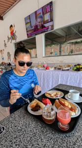 Vila do Walbinho في باريرينهاس: امرأة تجلس على طاولة مع طبق من الطعام +صورتان