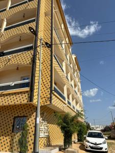 a yellow building with a white car parked next to it at Residence FATIMA in Thiès