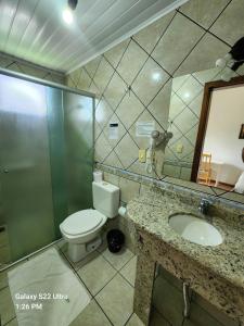 a bathroom with a toilet and a sink and a mirror at Hotel Vitoria in Videira