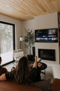 eine Frau, die auf einer Couch liegt und im Wohnzimmer fernsieht in der Unterkunft Forest Refuge - Fire - HotTub - Tremblant 15 min in La Conception