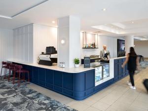 a woman walking past a blue counter in a restaurant at Mercure Brisbane Garden City in Brisbane