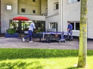 two men walking past a ping pong table with a red umbrella at Ibis Orly Chevilly Tram 7 in Chevilly-Larue