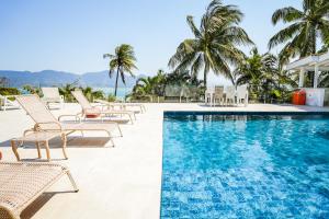 uma piscina em um resort com cadeiras e palmeiras em VELINN Pousada Casa da Imperatriz em Ilhabela