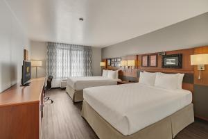 a hotel room with two beds and a desk at Clarion Inn Salt Lake City Airport in Salt Lake City