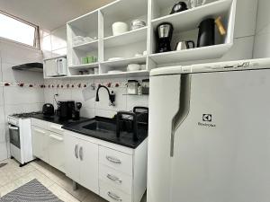 a white kitchen with a sink and a refrigerator at Kitnet vista Mar, pé na areia – Guilhermina in Praia Grande