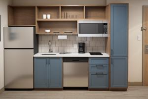 a small kitchen with blue cabinets and a refrigerator at Candlewood Suites Chatham South by IHG in Chatham
