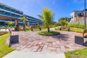 a park with benches and palm trees in front of a building at Beach Class Summer resort condominium by Carpediem in Porto De Galinhas