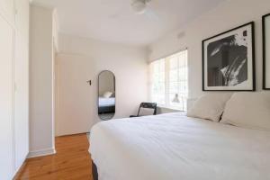 a white bedroom with a bed and a mirror at Gem Apartment 4 - Courtyard I Beach I Wifi I Cafes in Glenelg