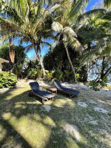 twee stoelen en een tafel op een strand met palmbomen bij Maree's Beachfront House - Free Internet in Arorangi