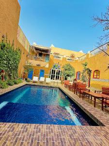a swimming pool in front of a building with benches at La Petite Kasbah in Zagora