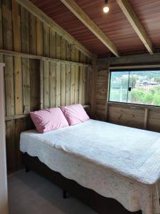 a bed with pink pillows in a wooden room at Apartamento de 2 Quartos para 4 Pessoas - 5 min da Praia in Garopaba