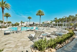 a pool at a resort with chairs and palm trees at Settle By The Sea in Inlet Beach