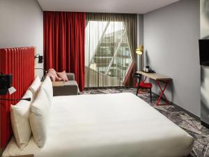 a hotel room with a large bed and a red curtain at ibis Styles London Ealing in London