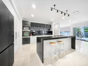 a kitchen with black and white appliances and stools at Relaxed Luxury for Families by the Beach in Buddina