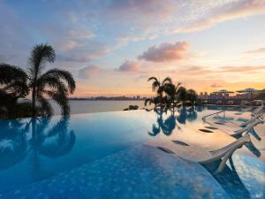 a resort swimming pool with palm trees and a sunset at 珠海凤凰湾悦榕庄 in Zhuhai