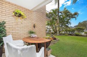 een patio met een houten tafel en witte stoelen bij Chambers River Retreat in Maroochydore
