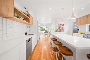 a kitchen with white counters and wooden stools at The Palma your Leafy Tropical Escape in Moffat Beach in Caloundra