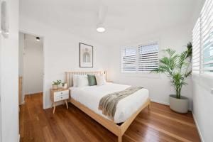 a white bedroom with a bed and a plant at The Palma your Leafy Tropical Escape in Moffat Beach in Caloundra