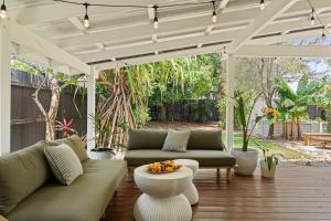 a patio with couches and a table on a wooden floor at The Palma your Leafy Tropical Escape in Moffat Beach in Caloundra