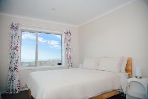 a white bedroom with a large bed and a window at Hilltop Ocean Hideaway - Aotea Wellington in Porirua +24 photos